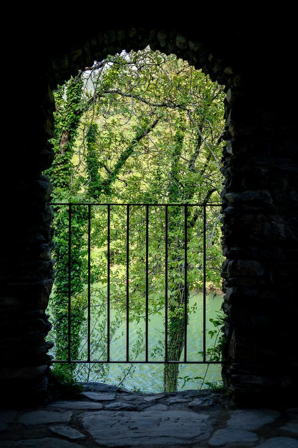 Stone archway and iron railing opening onto green trees and water