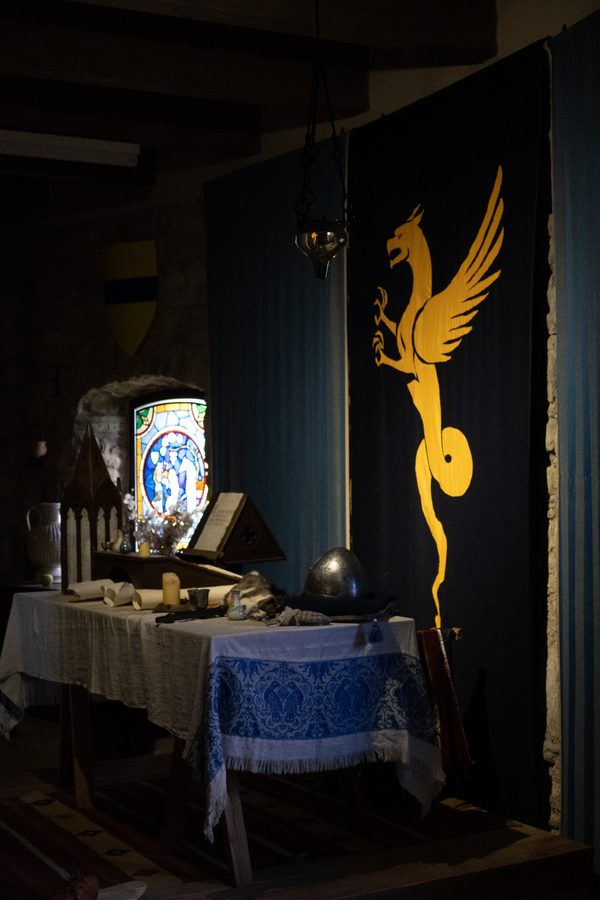 Dark historic interior with a yellow griffin banner and table objects