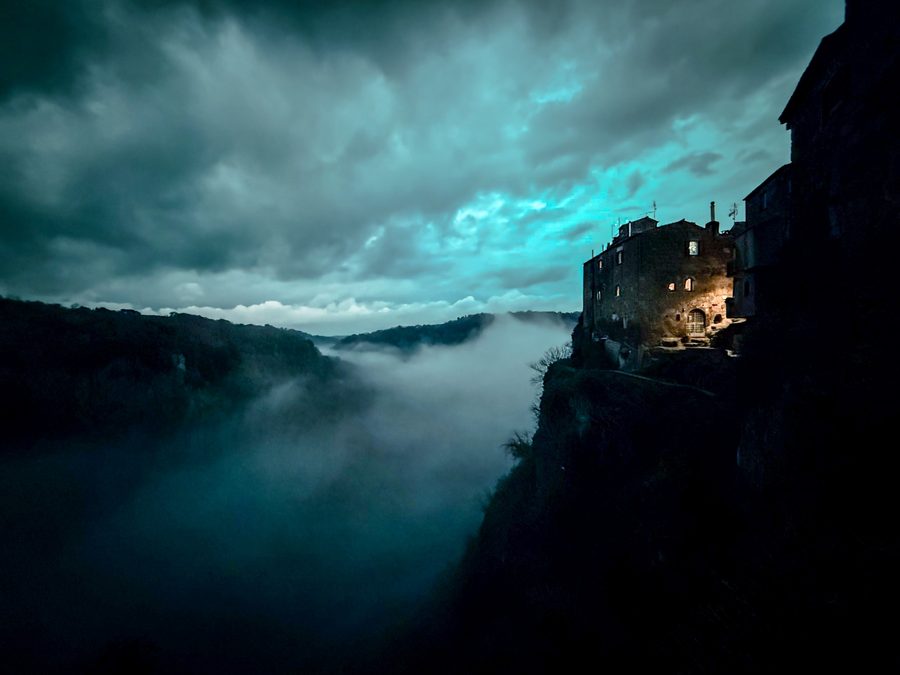 Moody village on a cliff with blue storm clouds and fog