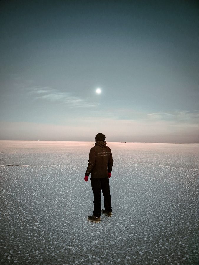 Solitary figure standing on a frozen surface under pale light