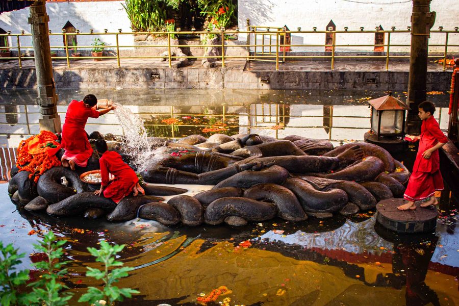 Children in red clothing performing a ritual gesture near water
