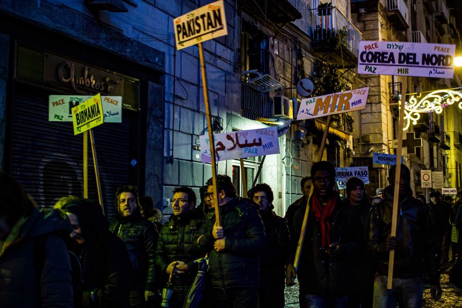 Night street demonstration with people holding multilingual peace signs