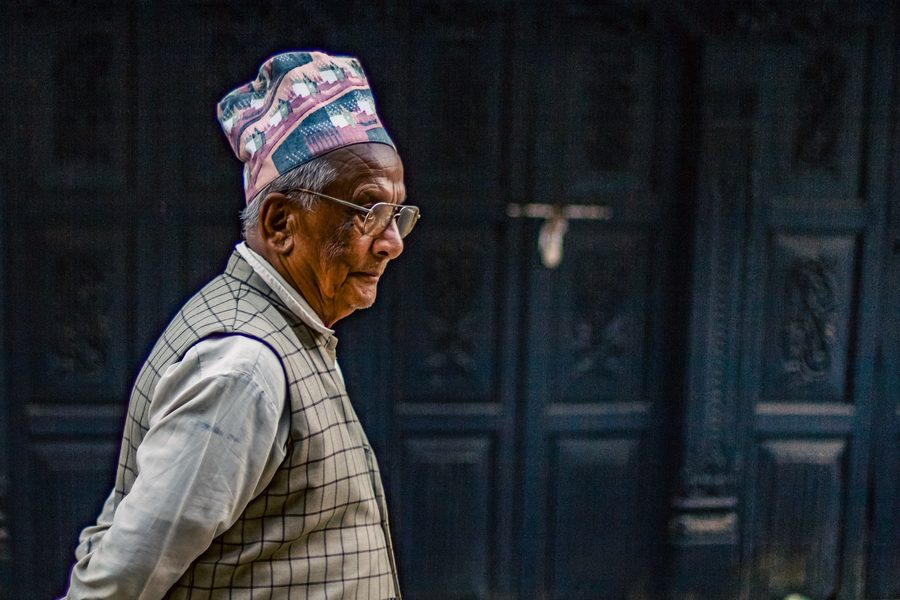 Profile portrait of an older man in a patterned cap against a dark wall