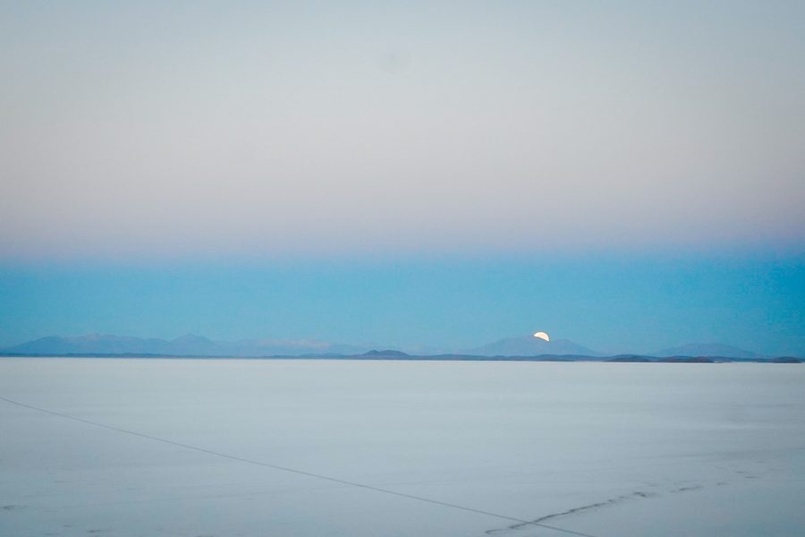 Minimal salt flat landscape with a pale moon rising over distant mountains