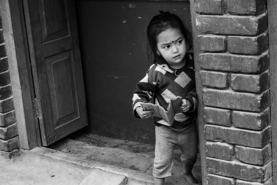 Black and white photograph of a child standing at a doorway beside a brick wall